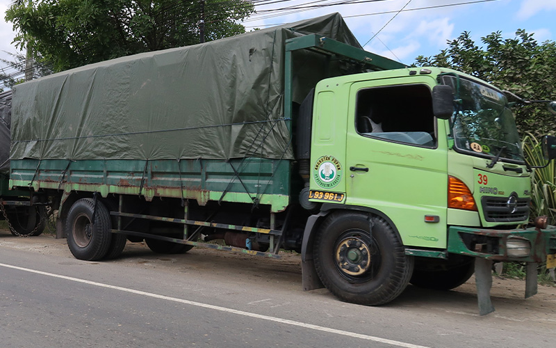 A light green Hino commercial truck with a dark green tarp-covered cargo bed parked along a roadside.